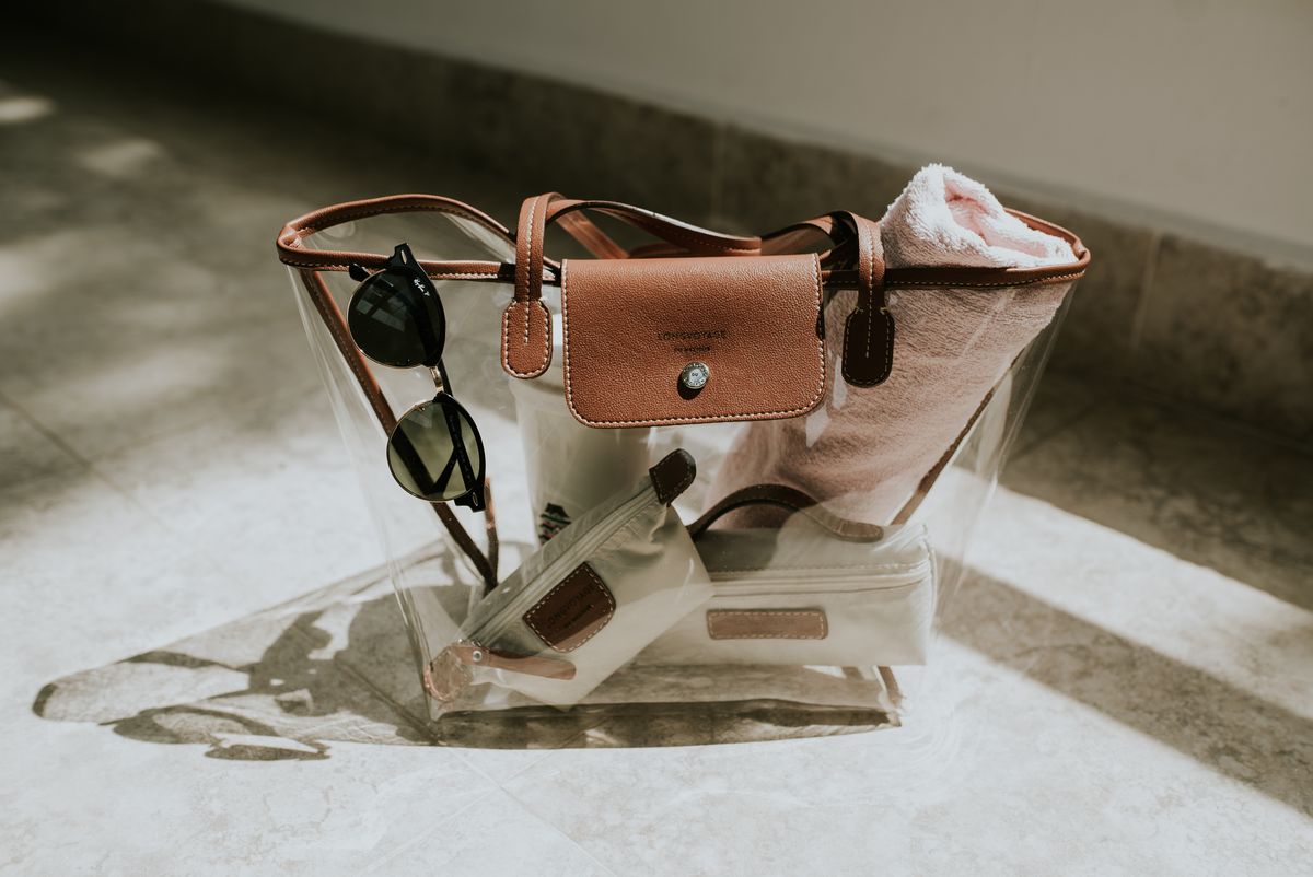A clear handbag with leather accents, sunglasses, and a towel, capturing a sunny day indoors.