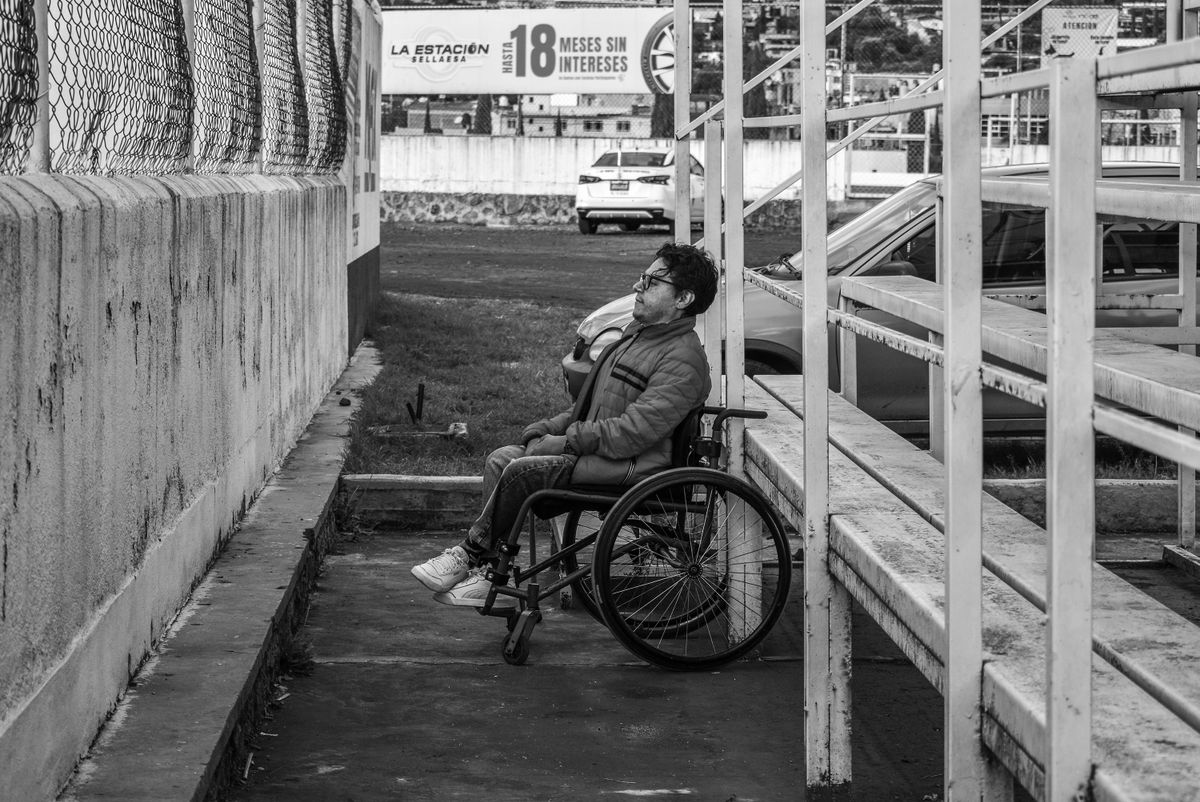 Black and white photo of a man in a wheelchair near stadium stands in Atlacomulco, Mexico.