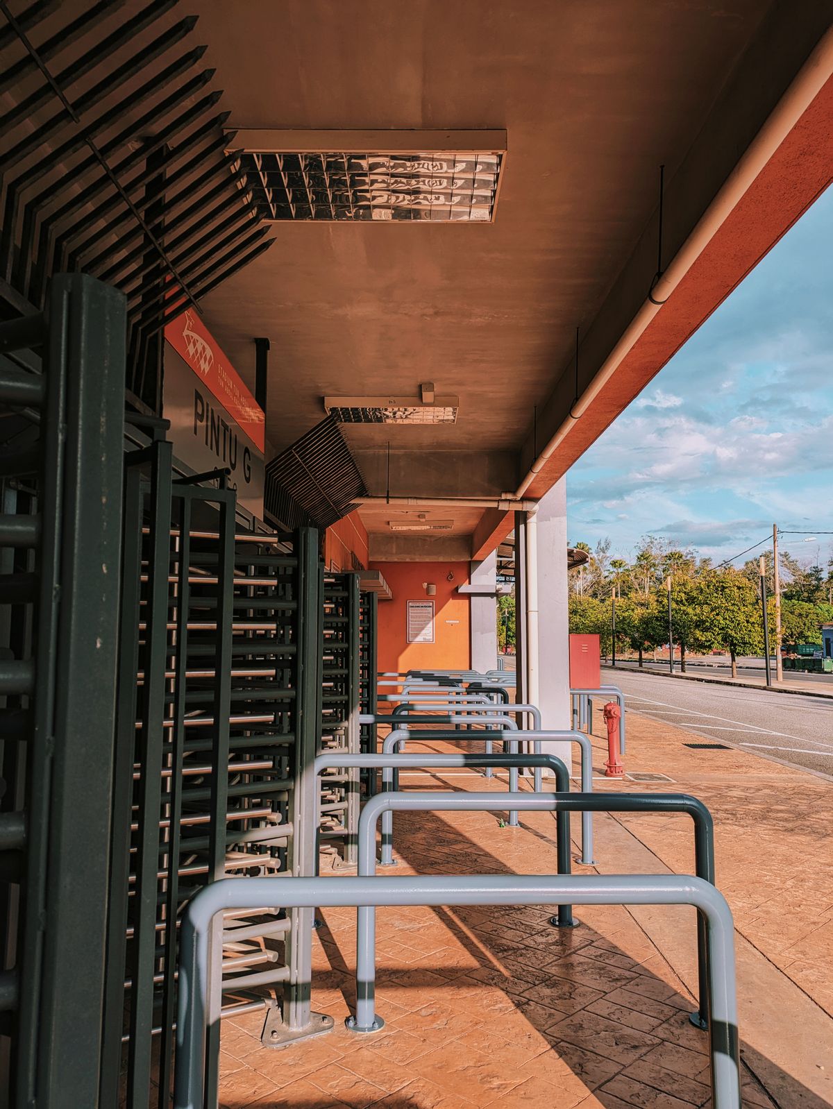 Minimalist photo of a stadium entrance with turnstiles and afternoon shadows under a bright sky.